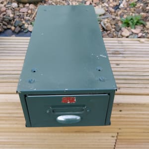 May include: A dark green metal filing cabinet with a single drawer. The drawer has a silver handle and a red label that says "CHICAGO" in white letters.