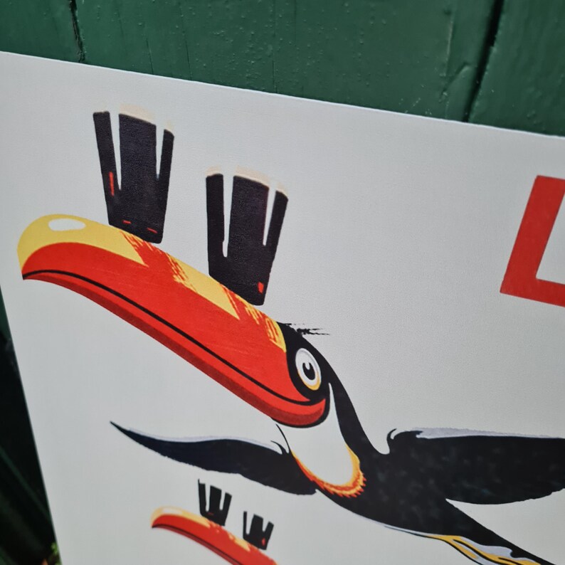 May include: A white poster with a cartoon toucan design. The toucan has a large red and yellow beak, black wings, and is accompanied by images of dark beer glasses. The letter "L" is visible in the upper right corner.