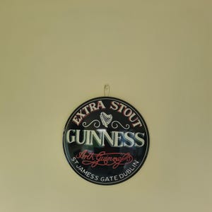 May include: A round Guinness Extra Stout sign with a black background and white and red lettering. The sign features a harp symbol and the text "St James Gate Dublin."