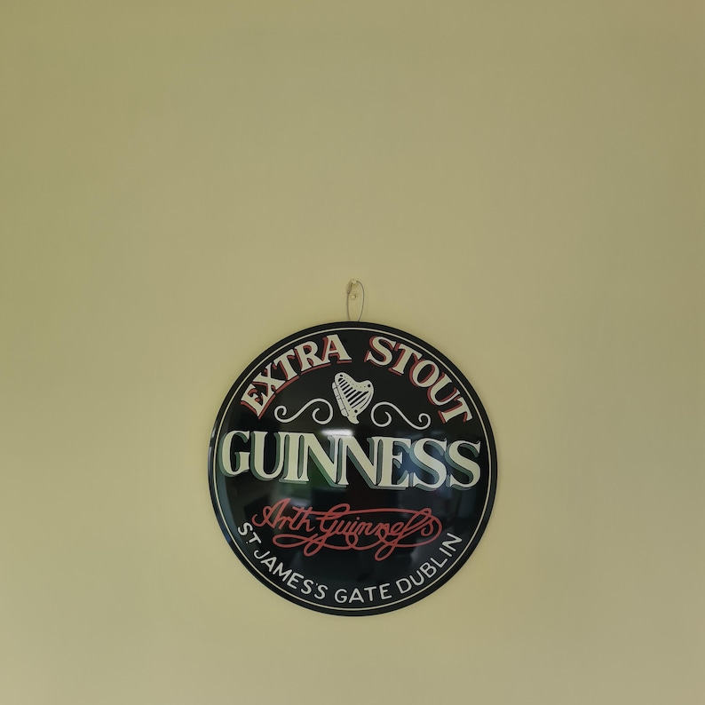 May include: A round Guinness Extra Stout sign with a black background and white and red lettering. The sign features a harp symbol and the text "St James Gate Dublin."