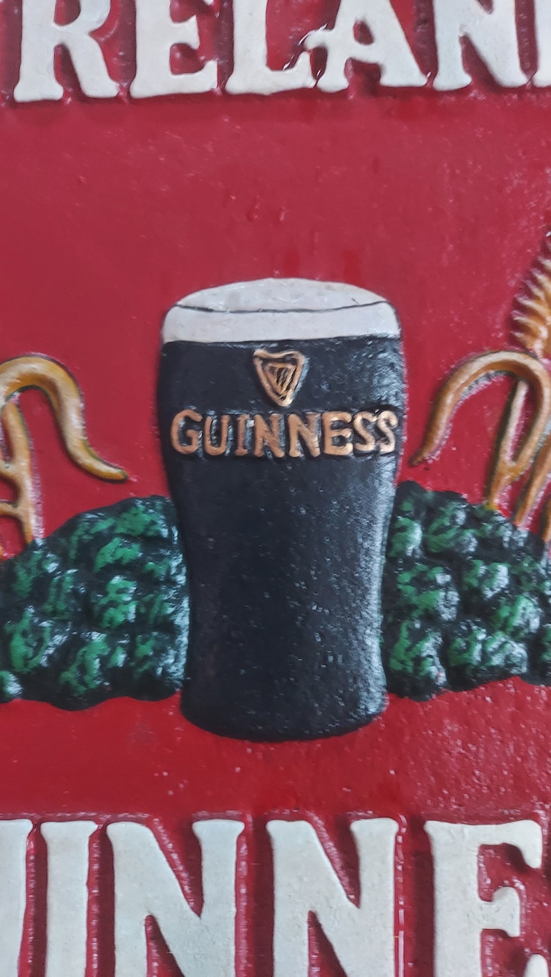 May include: A red sign with the word "IRELAND" at the top and "GUINNESS" in gold lettering on a black pint glass. The sign has green foliage and gold accents, with the word "INN" at the bottom.