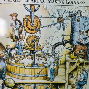 May include: A cartoon illustration depicting the process of making Guinness beer. The illustration shows a series of workers using a complex system of gears, pipes, and a large wooden vat to create the beer. The text "The Gentle Art of Making Guinness" is at the top of the image.