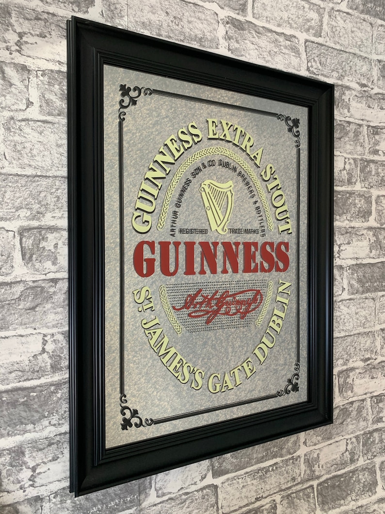 May include: A framed mirror with a vintage Guinness Extra Stout advertisement. The mirror has a black frame and a silver background with a gold rope design. The text on the mirror reads "GUINNESS EXTRA STOUT", "ARTHUR GUINNESS SON & CO. DUBLIN BREWERS & BOTTLERS", "REGISTERED", "TRADEMARKS", "GUINNESS", "ST. JAMES'S GATE DUBLIN".