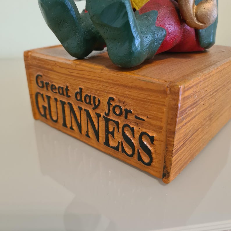 May include: Wooden decorative box with the text "Great day for Guinness" in black lettering. The box has a light brown finish and is slightly distressed. The top of the box has a figure with green shoes, red pants, and a yellow shirt.