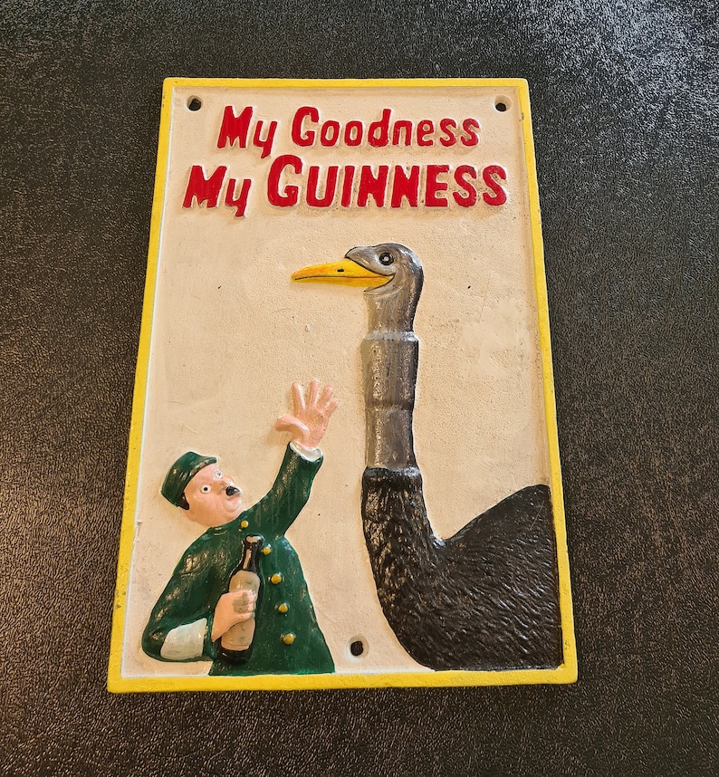 K&ouml;nnte beinhalten: Ein Vintage-Schild aus Gusseisen mit gelbem Rand. Das Schild zeigt eine Cartoon-Illustration eines Mannes, der eine Flasche Guinness-Bier h&auml;lt, und eine Strau&szlig; mit dem Text "My Goodness My Guinness".