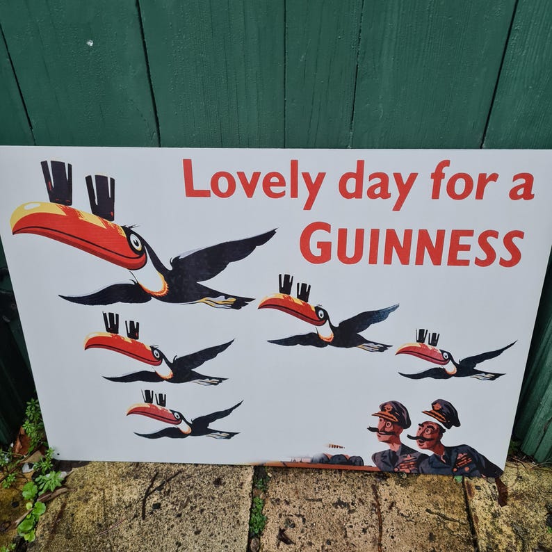 May include: A vintage Guinness advertisement featuring toucans with red and yellow beaks, black wings, and small hats. The text reads "Lovely day for a Guinness" in red. Two men in military uniforms are also depicted.