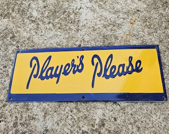 May include: A rectangular sign with a yellow center and a blue border. The words "Players Please" are written in cursive blue font across the center of the sign. The sign has visible screw holes.