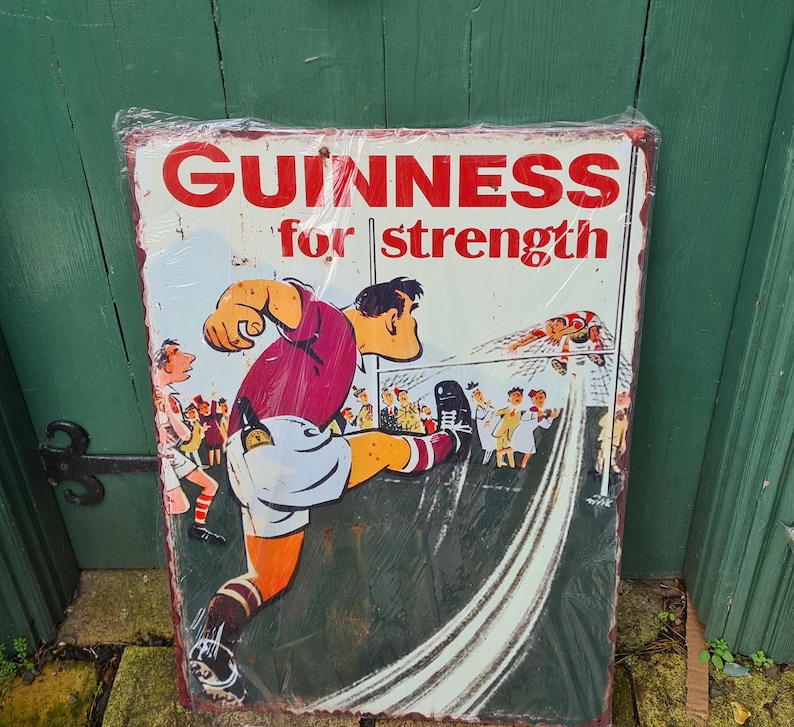 May include: Vintage metal sign advertising Guinness beer with the text "Guinness for strength". The sign features a cartoon illustration of a man kicking a football.