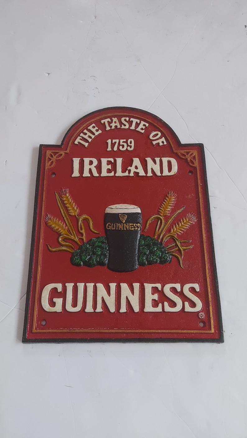 May include: Red and gold metal sign with the text "THE TASTE OF IRELAND 1759 GUINNESS". The sign features a pint of Guinness, wheat stalks, and hops.