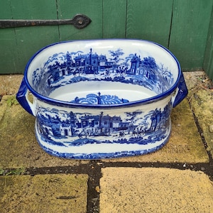 May include: A white ceramic planter with blue and white floral designs. The planter has two handles on the sides and is oval shaped.