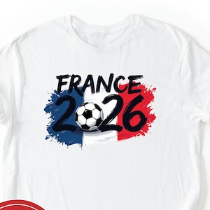 May include: White t-shirt featuring the text "FRANCE 2026" in black, with a soccer ball graphic. The design incorporates the French flag colors: blue, white, and red. A red circle with the text "NEXT DAY SHIPPING" is in the lower left.