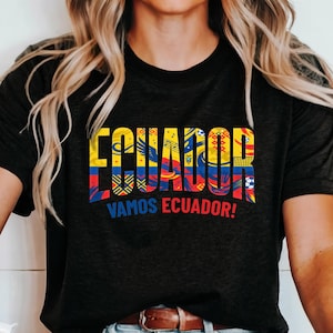May include: A black short-sleeved t-shirt featuring the word ECUADOR in large yellow, blue, and red block letters filled with patterns including soccer balls and national symbols, with the text VAMOS ECUADOR! printed in blue and red below.