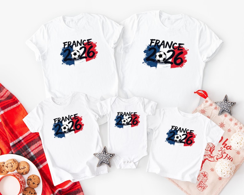 K&ouml;nnte beinhalten: Wei&szlig;e T-Shirts mit einem Fu&szlig;ball-Grafik und dem Text "FRANCE 2026" in Schwarz. Die Grafik enth&auml;lt die Farben der franz&ouml;sischen Flagge: Blau, Wei&szlig; und Rot. Die Shirts sind in verschiedenen Gr&ouml;&szlig;en erh&auml;ltlich, darunter ein Body.