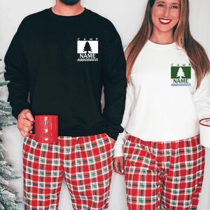 Puede incluir: Dos sudaderas, una negra y otra blanca, con un dise&ntilde;o de &aacute;rbol y las palabras "CAMP" y "NAME". Se combinan con pantalones de pijama a cuadros rojos. Uno sostiene una taza roja, el otro un recipiente blanco.