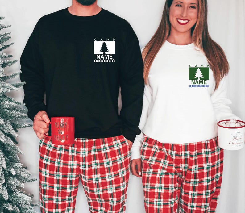 Puede incluir: Dos sudaderas, una negra y otra blanca, con un dise&ntilde;o de &aacute;rbol y las palabras "CAMP" y "NAME". Se combinan con pantalones de pijama a cuadros rojos. Uno sostiene una taza roja, el otro un recipiente blanco.