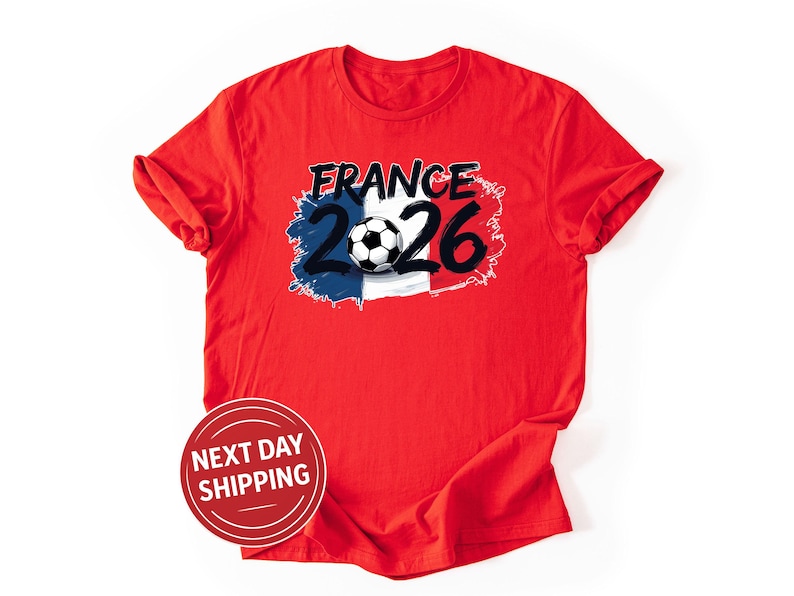 K&ouml;nnte beinhalten: Rotes T-Shirt mit einem Grafikdesign. Das Design enth&auml;lt das Wort "FRANCE" in Schwarz, die Zahl "26" und einen Fu&szlig;ball. Das Design integriert die Farben der franz&ouml;sischen Flagge: Blau, Wei&szlig; und Rot. Rundhalsausschnitt.