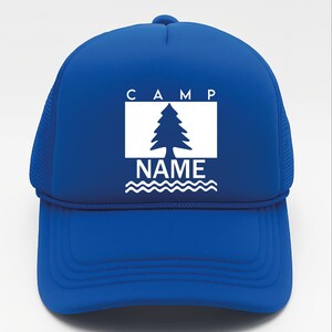 May include: A royal blue trucker hat with a white graphic. The graphic features the word "CAMP" above a white rectangle with a pine tree silhouette, the word "NAME" below, and wavy lines. The hat has a mesh back.