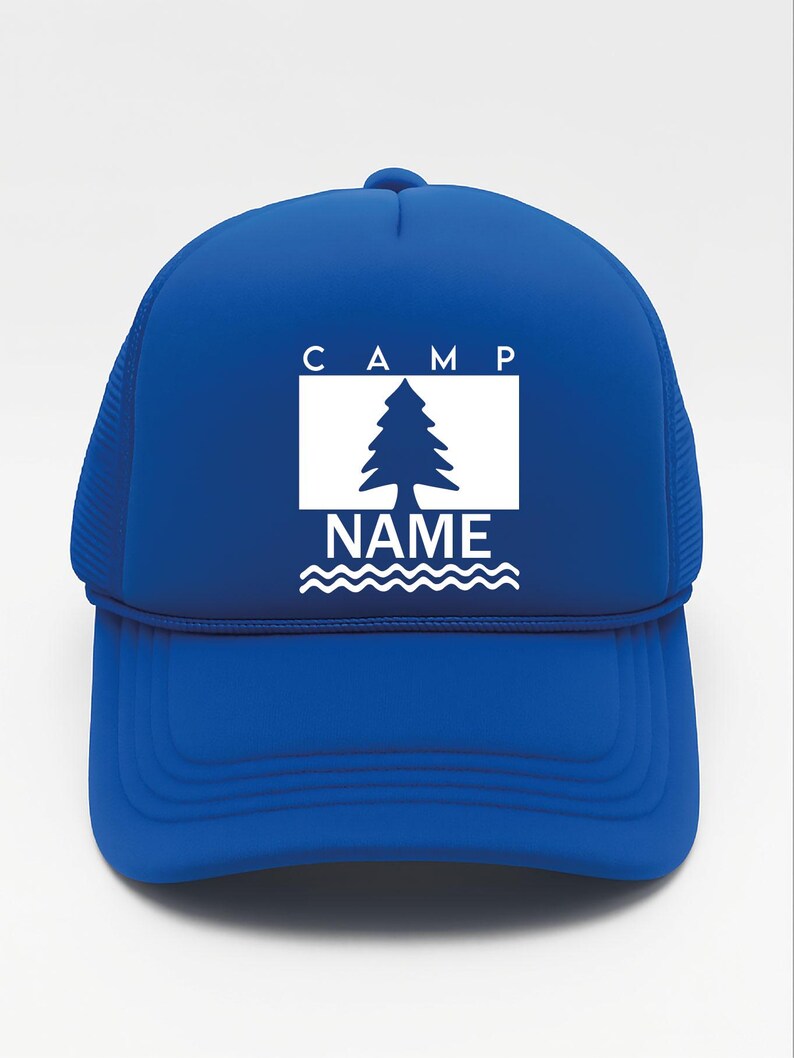 May include: A royal blue trucker hat with a white graphic. The graphic features the word "CAMP" above a white rectangle with a pine tree silhouette, the word "NAME" below, and wavy lines. The hat has a mesh back.