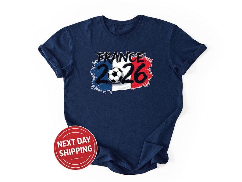 K&ouml;nnte beinhalten: Marineblaues T-Shirt mit einem Aufdruck "FRANCE 2026" &uuml;ber einem Fu&szlig;ball, vor dem Hintergrund der franz&ouml;sischen Flagge. Das Design ist in Wei&szlig;, Rot und Blau gehalten. Ein roter Kreis mit dem Text "NEXT DAY SHIPPING" befindet sich unten links.