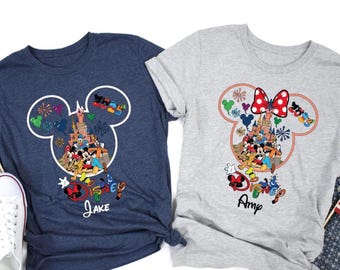 May include: Two t-shirts, one navy blue and one gray, each featuring a Mickey Mouse head outline with a castle and Disney characters inside. The navy shirt has the name "Jake" and the gray shirt has the name "Amy".