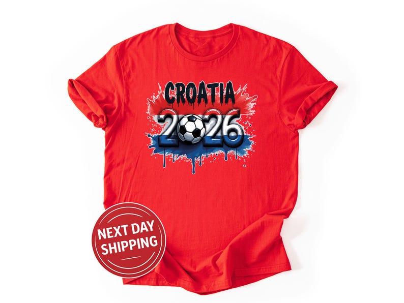 May include: A red t-shirt featuring the word "CROATIA" above the numbers "2026" with a soccer ball in the center. The design incorporates red, white, and blue colors, with a dripping paint effect. The shirt is made of a soft material.