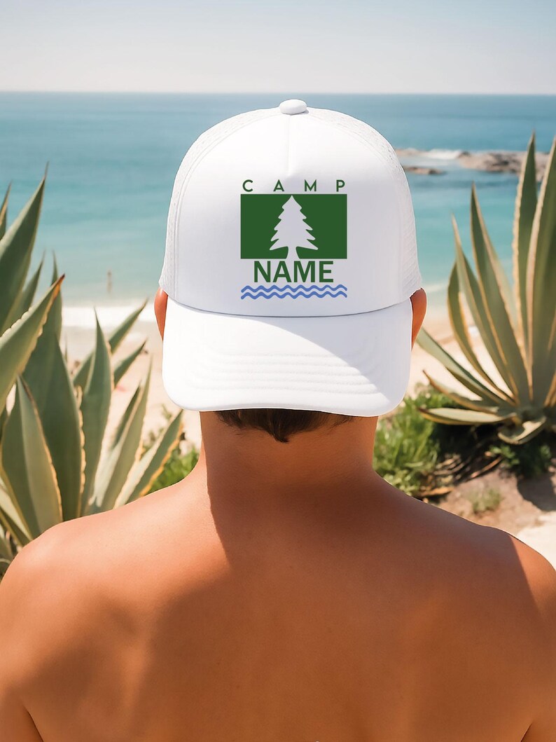 May include: White trucker hat featuring a green square with a tree graphic, the word "CAMP" above and "NAME" below. Blue wavy lines are at the bottom of the graphic. The hat is worn by a person with a beach background.