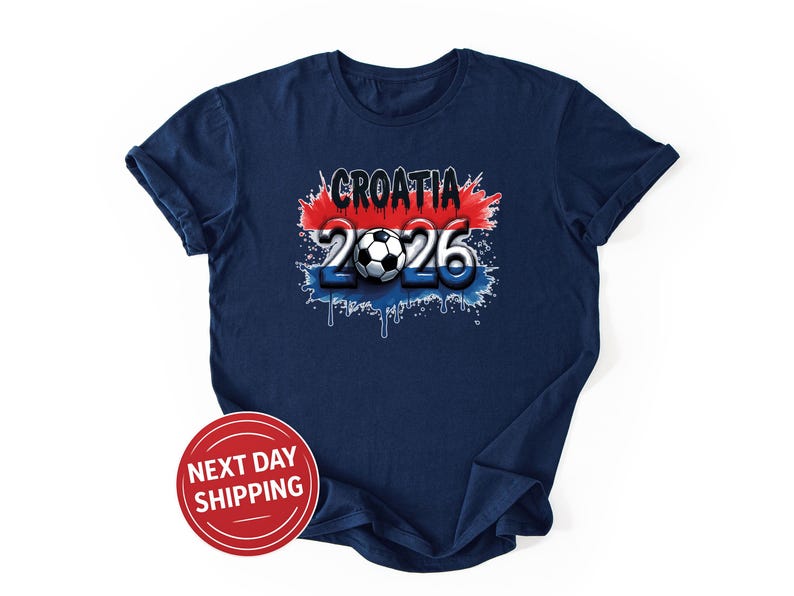 May include: Navy blue t-shirt with a graphic design featuring the word "CROATIA" in white, the number "2026", and a soccer ball. The design incorporates red, white, and blue colors, with a dripping paint effect. A red circle with "NEXT DAY SHIPPING" is also visible.