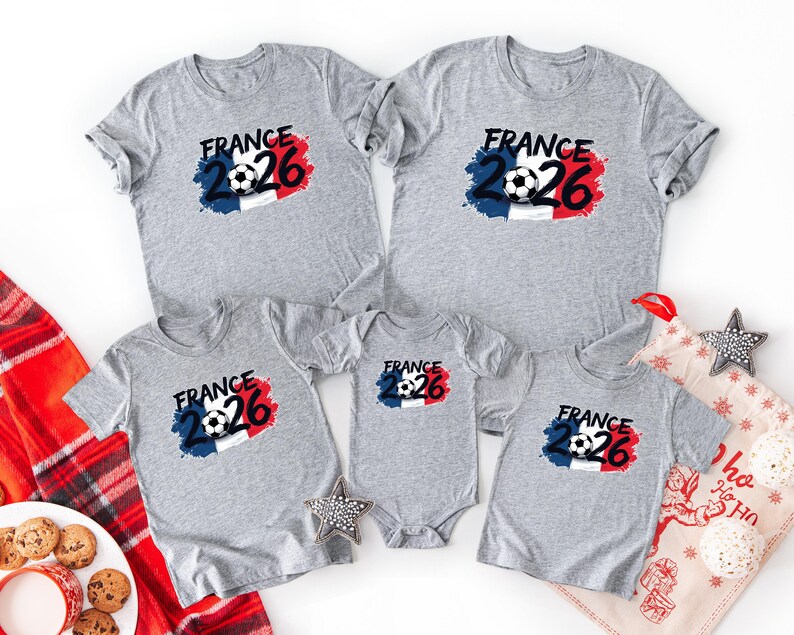 K&ouml;nnte beinhalten: Eine Auswahl grauer T-Shirts und ein Baby-Body mit einem Fu&szlig;ball-Design und dem Text "FRANCE 26" in Schwarz, Rot und Blau. Die Shirts sind kurz&auml;rmlig und eignen sich f&uuml;r eine Familie oder Gruppe.