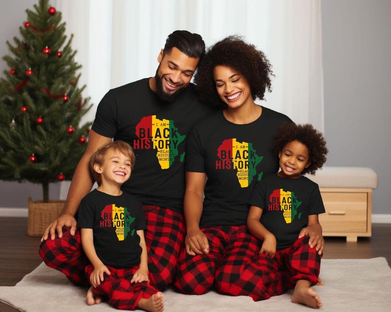 May include: A family of four wearing black t-shirts with a graphic of the continent of Africa in red, yellow, and green colors. The shirts have the text "I am Black History" on them. The family is sitting on a red and black plaid rug.
