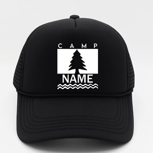May include: Black trucker hat with a white graphic. The graphic features the word "CAMP" above a tree inside a white rectangle, with the word "NAME" below, above wavy lines. The hat has a mesh back and a curved peak.