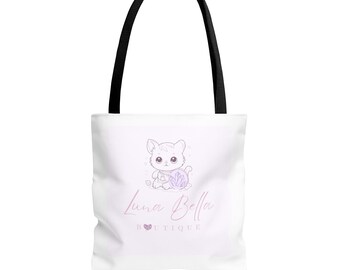 May include: White tote bag with black handles featuring a cute cartoon kitten holding a purple object. The bag has the text "Luna Bella Boutique" in a cursive font, with a heart symbol. The bag is designed for carrying items.