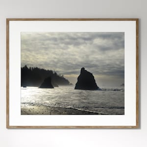May include: A framed photograph of a seascape with two rocky outcroppings in the distance. The sky is cloudy and the water is choppy. The photo is in a light wood frame.