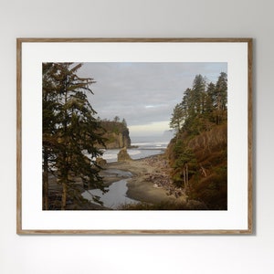 May include: A framed photograph of a scenic landscape with a rocky coastline, a river flowing through the sand, and lush green trees in the foreground. The sky is cloudy and the water is a light blue.
