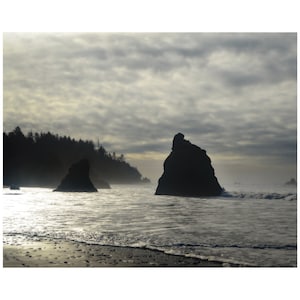 May include: Silhouetted rock formations rise from the ocean, with a cloudy sky overhead. The water is calm and reflects the light of the sky.