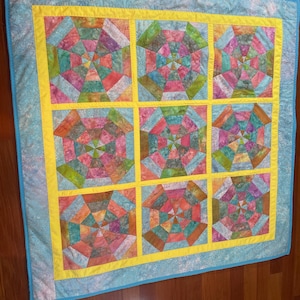May include: A colourful handmade quilt with a geometric design. The quilt features nine square blocks with a vibrant mix of pink, green, orange, and blue fabrics. A yellow border frames each block, and a light blue border surrounds the entire quilt.