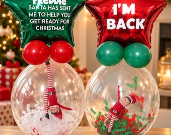Puede incluir: Dos globos transparentes con muñecos de elfo en su interior. El globo izquierdo contiene confeti blanco y una estrella verde con el texto: FREDDIE SANTA HAS SENT ME TO HELP YOU GET READY FOR CHRISTMAS. El derecho tiene confeti rojo/verde y una estrella roja: I'M BACK.
