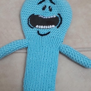 K&ouml;nnte beinhalten: Ein hellblaues, gestricktes Pl&uuml;schtier mit einem gro&szlig;en offenen Mund, schwarzen Augen und einer geschwungenen schwarzen Linie f&uuml;r ein L&auml;cheln. Das Spielzeug hat zwei ausgestreckte Arme und einen ausgestellten Sockel. Das Spielzeug ist eine Figur aus der Zeichentrickserie Rick and Morty.