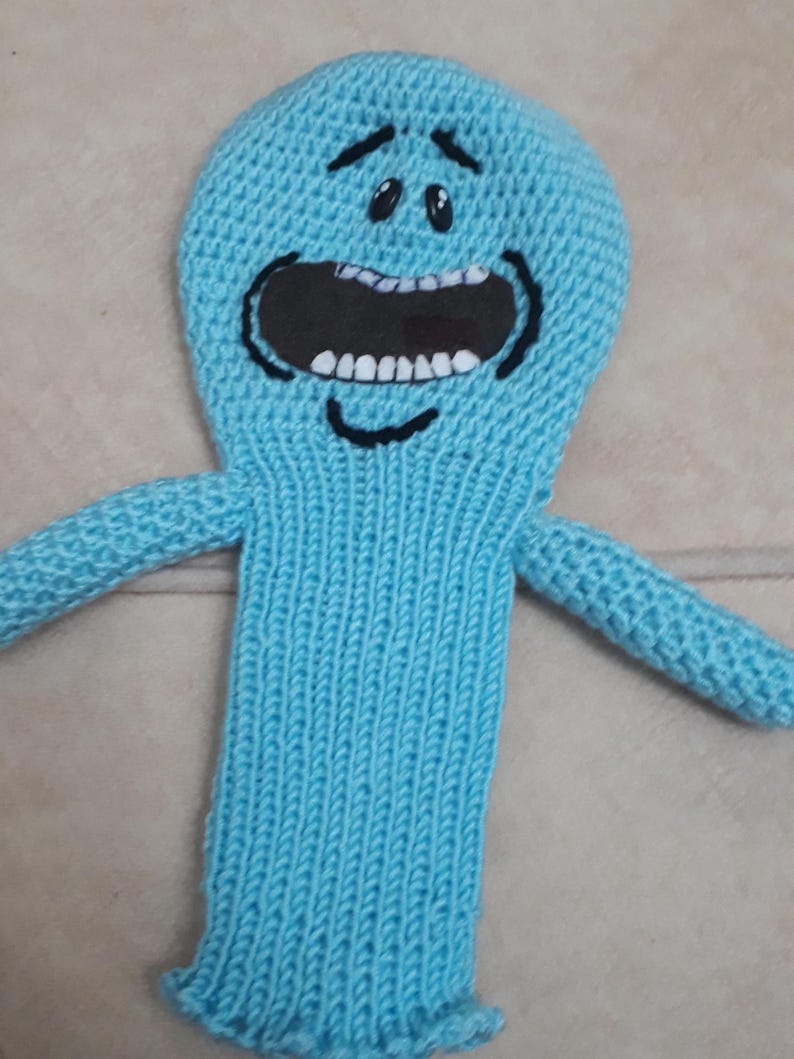 K&ouml;nnte beinhalten: Ein hellblaues, gestricktes Pl&uuml;schtier mit einem gro&szlig;en offenen Mund, schwarzen Augen und einer geschwungenen schwarzen Linie f&uuml;r ein L&auml;cheln. Das Spielzeug hat zwei ausgestreckte Arme und einen ausgestellten Sockel. Das Spielzeug ist eine Figur aus der Zeichentrickserie Rick and Morty.