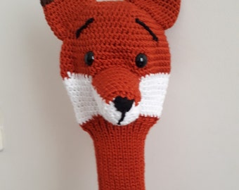 May include: A crocheted fox head golf club cover in orange, white, and brown. The fox has black eyes and a black nose.