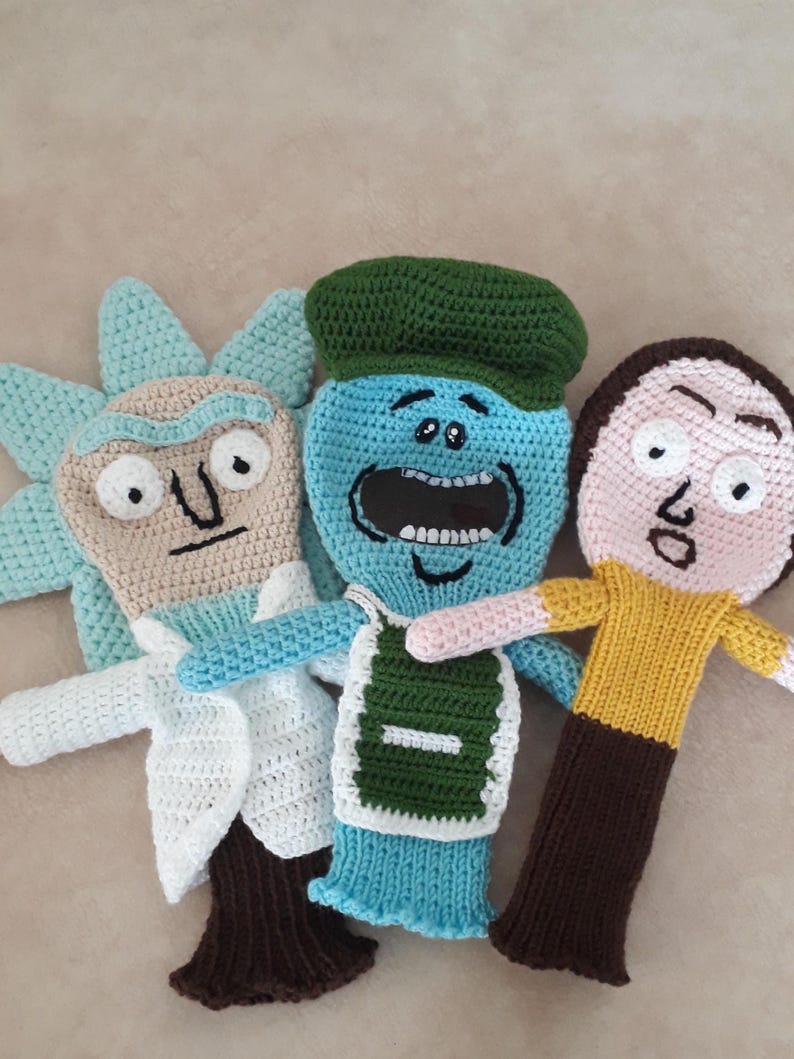 K&ouml;nnte beinhalten: Drei handgefertigte H&auml;kelpuppen, die jeweils eine Figur aus einer beliebten Zeichentrickserie darstellen. Die Puppen weisen unterschiedliche Gesichtsausdr&uuml;cke und Kleidungsdetails auf, darunter ein wei&szlig;er Laborkittel, eine gr&uuml;ne M&uuml;tze und ein gelbes Hemd. Die Puppen sind aus verschiedenen Garnfarben gefertigt.