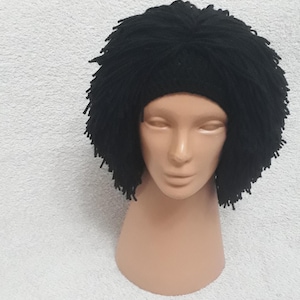 May include: A black yarn wig with a headband base, displayed on a mannequin head. The wig features a dense, textured design with short, spiky strands. The wig is designed to resemble a hairstyle.