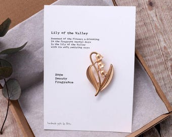 May include: A gold-toned lily of the valley brooch with a poem about the flower. The poem reads "Sweetest of the flowers a-blooming In the fragrant vernal days Is the lily of the Valley with its soft, retiring ways Hope Beauty Fragrance".