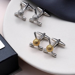 May include: Two pairs of cufflinks featuring a golf ball and clubs. One pair is silver with a white golf ball, and the other pair is gold with a gold golf ball.