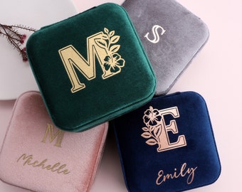 May include: Four square velvet jewelry boxes in shades of green, gray, pink, and navy blue. Each box features a gold initial and floral design. The pink box has the name "Michelle" and the navy box has the name "Emily".
