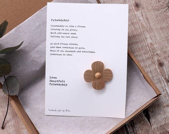 May include: A gold-colored flower pin with a poem about friendship on a white card. The poem reads: "Friendship is like a flower Glowing in its glory, Each and every seed, Telling its own story. As each flower blooms, And then continues to grow, More of its strength and knowledge, Continues to show. Love Heartfelt friendship"