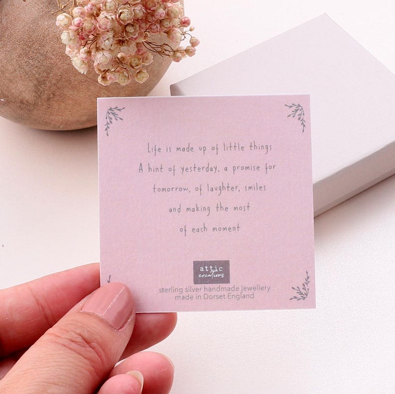 Puede incluir: Una tarjeta cuadrada de color rosa claro con el texto impreso: Life is made up of little things. A hint of yesterday, a promise for tomorrow, of laughter, smiles and making the most of each moment. La tarjeta incluye el logo Attic Creations.