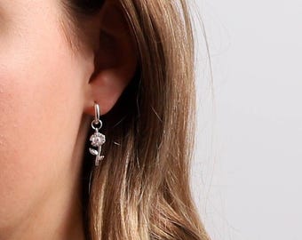 May include: Silver hoop earrings with a delicate flower charm dangling from the bottom.