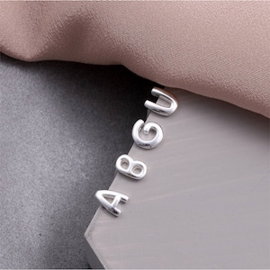 May include: Silver letter charms in the shape of the letters A, B, G, and U.