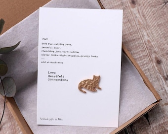 May include: A card with a poem about cats, featuring the text "Cat, Soft fur, swiping paws, peaceful purr. Clenching jaws, warm cuddles. Clever nooks, night snuggles, grumpy looks and so much more Love Heartfelt Connections handmade gifts by Atti" and a gold metal cat cutout.