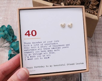 May include: A small gift box with a white card inside. The card has a red number 40 printed on it and a message about celebrating 40 years. The box also contains a pair of small gold heart-shaped earrings with clear stones.